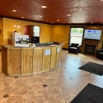 Hotel lobby featuring a curved wooden front desk, yellow walls, and a cozy fireplace seating area.