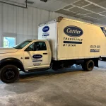 White refrigerated box truck with Carrier Transicold logos inside a garage.
